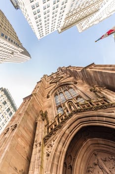 Wide angle upward view of Trinity Church at Broadway and Wall Street with surrounding skyscrapers, Lower Manhattan, New York City, USA.