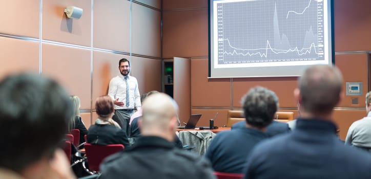 Public Speaker Giving a Talk at Business Meeting. Audience in the conference hall. Skilled coach answers questions of participants of business training. Business and Entrepreneurship concept.
