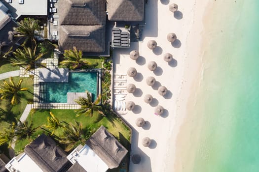 Aerial view of beautiful tropical beach front hotel resort with swimming pool, palm leaves umbrellas and turquoise sea. Paradise destination for vacations in Mauritius.