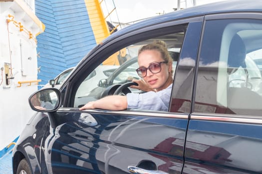 Female driver parking her car on ferry boat on trip to their summer vacations island destination. Sardinia, Italy. Water transport concept.