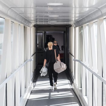 Airplane Boarding. Casual female passenger carrying the hand luggage bag, walking the airplane boarding corridor.