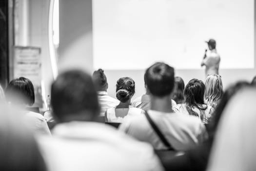 Speaker giving a talk in conference hall at business event. Focus on unrecognizable people in audience. Business and Entrepreneurship concept. Black and white image.