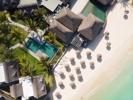 Aerial view of beautiful tropical beach front hotel resort with swimming pool, palm leaves umbrellas and turquoise sea. Paradise destination for vacations in Mauritius.