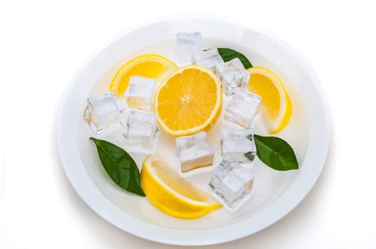 lobes of fresh, bright, yellow lemon, cubes of refreshing ice and green leaves on a plate on a white background. isolated.