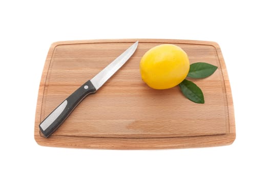 yellow lemon with green leaves and a knife on a wooden cutting board.