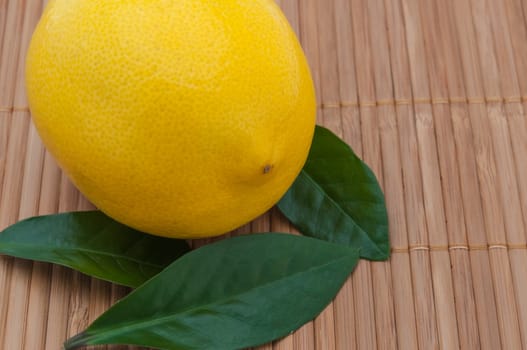 yellow lemon with green leaves close-up on bamboo mat.