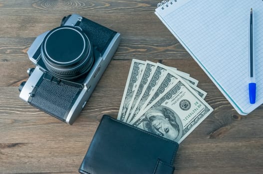 Retro camera, purse and notepad with pen on a wooden table.