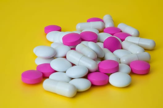 A pile of pills of different colors on a yellow background.