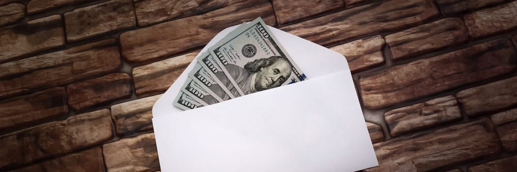 White envelope with five hundred dollar bills in a ray of light against a dark brick wall.