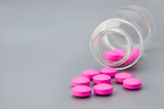 Pink large pills scattered from a glass jar on a gray background.