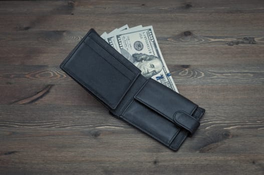 Opened black purse with bills of one hundred dollars on a table.