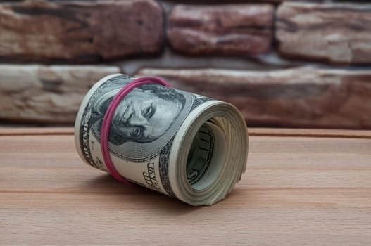 a bundle of American dollar bills on a wooden table near a brick wall.