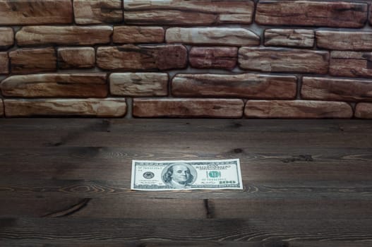 On a dark wooden table near a brick wall of a bill one hundred dollars.