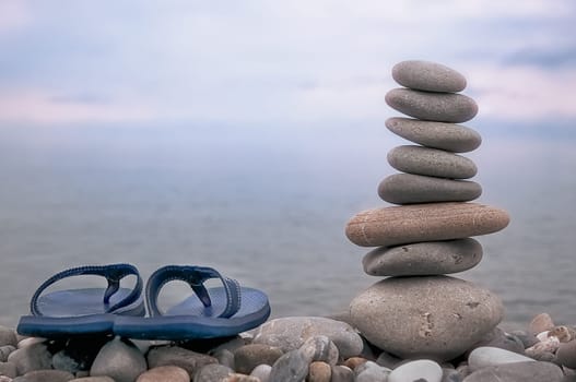 Rocky beach, heavy sky, sea, slippers and a pyramid of gray stones.