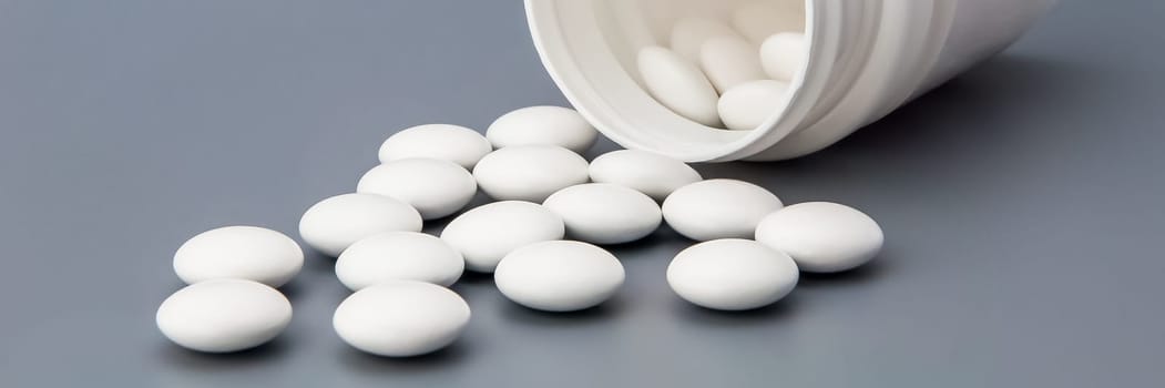 White round pills scattered from a white jar.