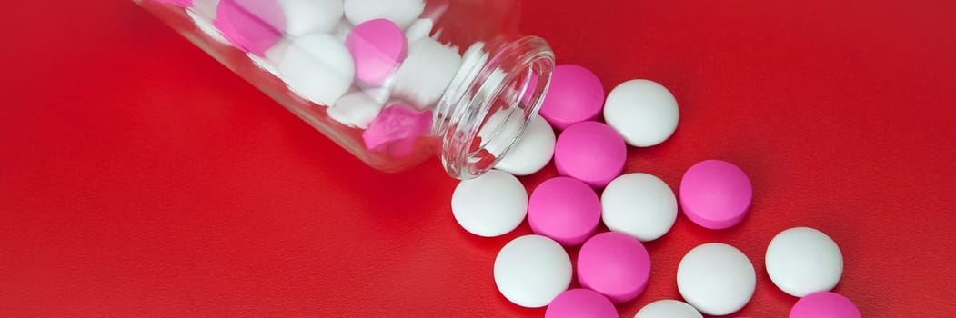 Pink and white pills scattered from a glass jar on a red background.