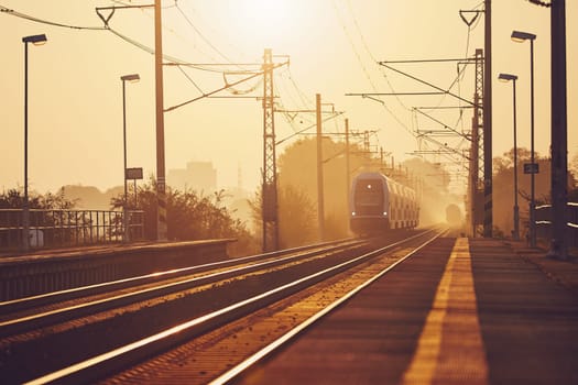 Passenger train commuting to railroad station at golden sunrise.