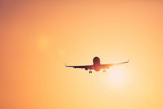 Low angle view airplane landing against golden sky at sunset.
