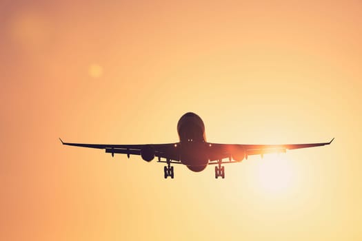 Low angle view airplane landing against golden sky at sunset.