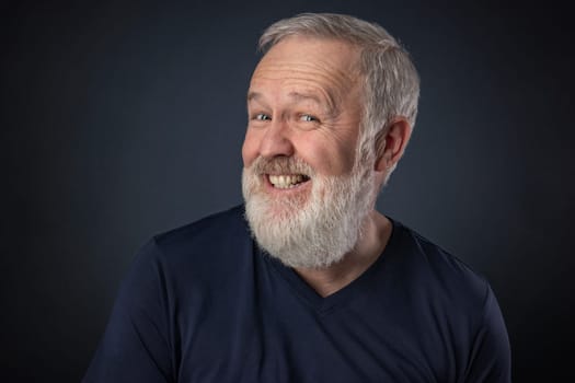 Old man portrait with gray beard on blue background playing and pretending to laugh