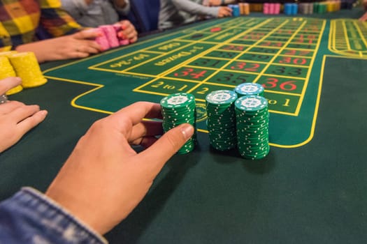Casino, gambling and entertainment concept - male hand with stack of poker chips on a green table background