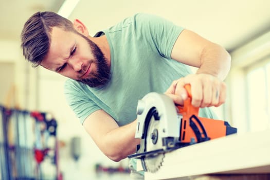 young worker with hand saw in a carpenter's workshop
