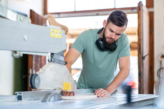 young worker using saw in a carpenter's workshop