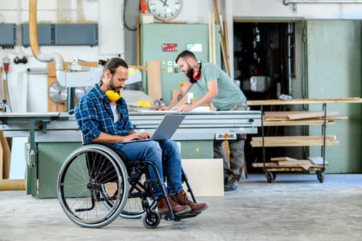 disabled worker in wheelchair in a carpenter's workshop with his colleague