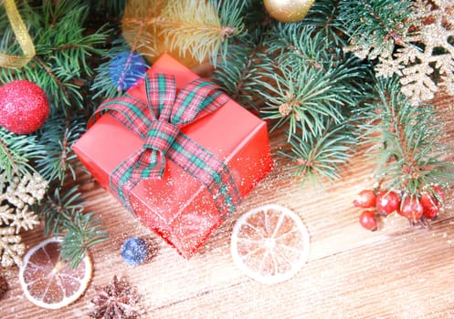 Christmas or winter decoration background. Christmas red gift box with sparkling christmas tree branches and xmas balls on a rustic wooden table. Closeup.