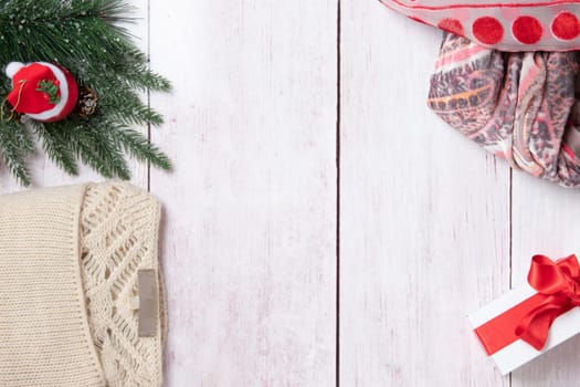 Christmas or winter decoration background. Compostion from christmas tree branches, winter sweater, scarf and a xmas gift box on a wooden table. Space for design. Top view.