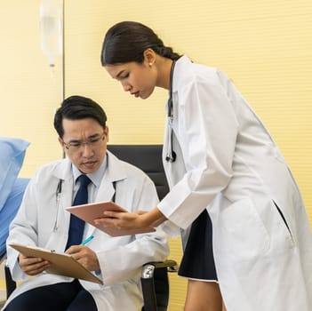Two Asian Doctors make discussion while routine health check with patient in hospital ward