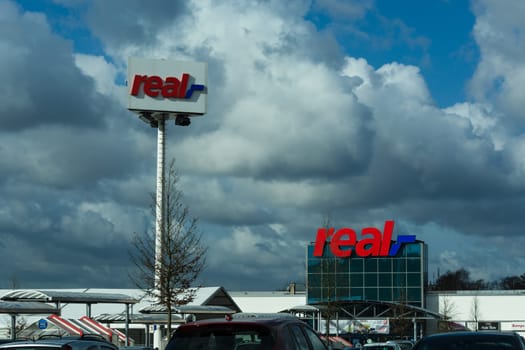 HEILIGENHAUS, NRW, GERMANY - FEBRUARY 24, 2017: Real logo on department store in Heiligenhaus in front of a dramatic sky. Real Warehouse is a German trading chain..