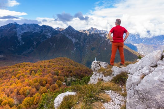 Senior hiker standing on top and admiring the mountains landscape with forest in autumn colors.