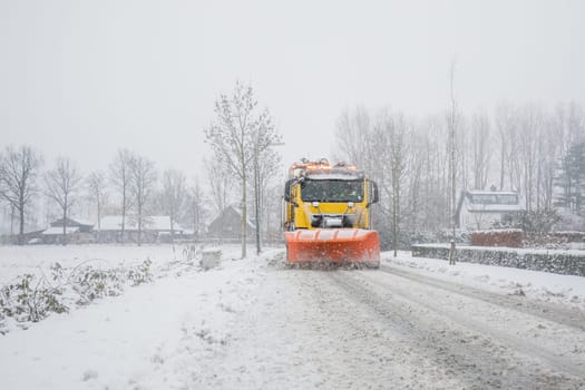 Snowplow removes snow off icy road in winter