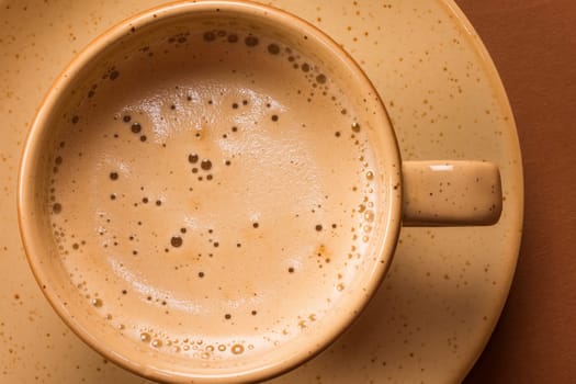 Cup of coffee or cappuccino in beige mug on brown background.
