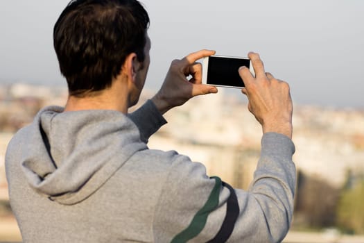 The tourist is using mobile phone for taking a picture about city.
