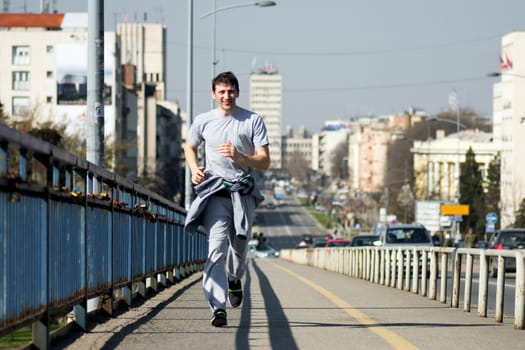 The smiling man is jogging on the bridge in the city.