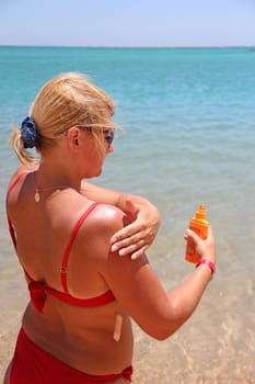 Young woman is smeared with protective cream during exotic vacation. Blonde woman using cream during sunbathing. Attractive woman with healthy skin applying sunscreen to shoulder. Skincare