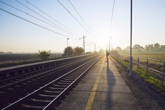 Alone young man with backpack waiting for train at railroad station at sunrise.