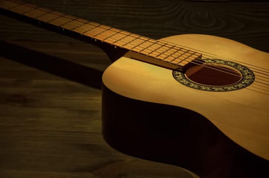 The acoustic guitar lies on a wooden table in the dark, a beam of light illuminates it.