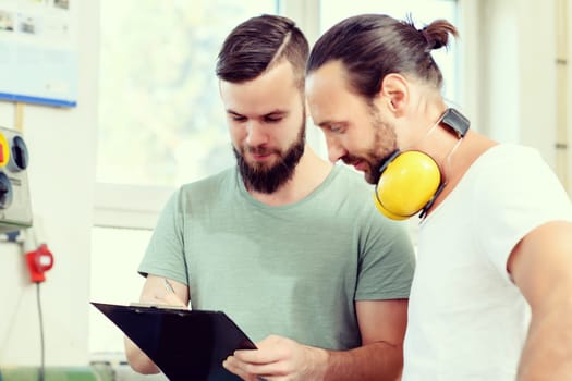 two men in workwear with clipboard in a carpenter's workshop