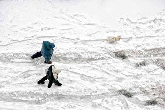 Elevated view of man and woman couple walking with dog on frozen snow covered street in winter