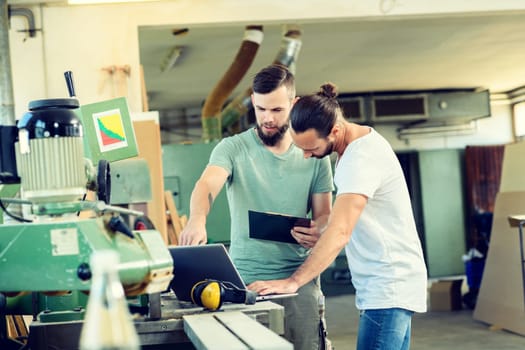 two worker in a carpenter's workshop with clipboard and computer