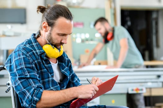 disabled worker in wheelchair in a carpenter's workshop with his colleague