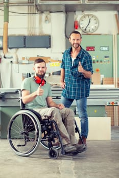 disabled worker in wheelchair in a carpenter's workshop with his colleague showing thumb up