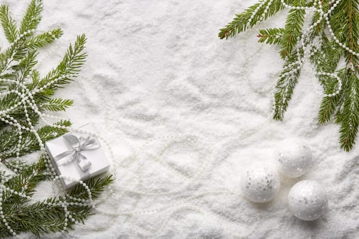 Fir tree branches with decorations and gift box on a snow background with copy space. Top view. Christmas and New Year. Winter holiday. Greeting card
