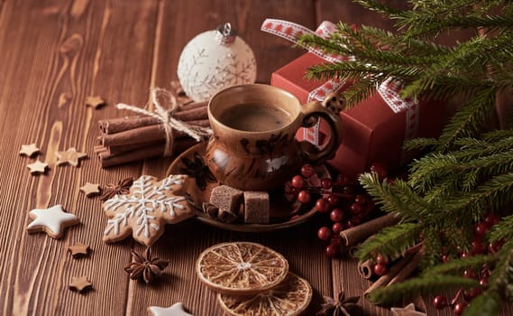 Cup of coffee, gingerbread cookies, gift box, fir tree branches with decorations on a wooden brown background. Christmas and New Year treat.