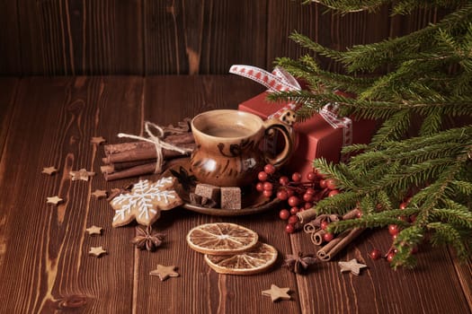Cup of coffee, gingerbread cookies, gift box, fir tree branches with decorations on a wooden brown background. Christmas and New Year treat.