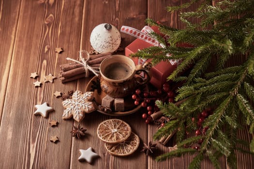 Cup of coffee, gingerbread cookies, gift box, fir tree branches with decorations on a wooden brown background. Christmas and New Year.Top view.