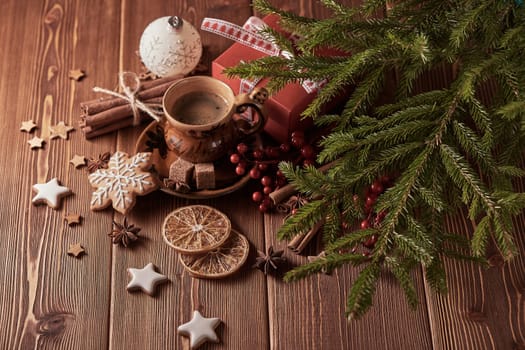 Cup of coffee, gingerbread cookies, gift box, fir tree branches with decorations on a wooden brown background. Christmas and New Year.Top view.